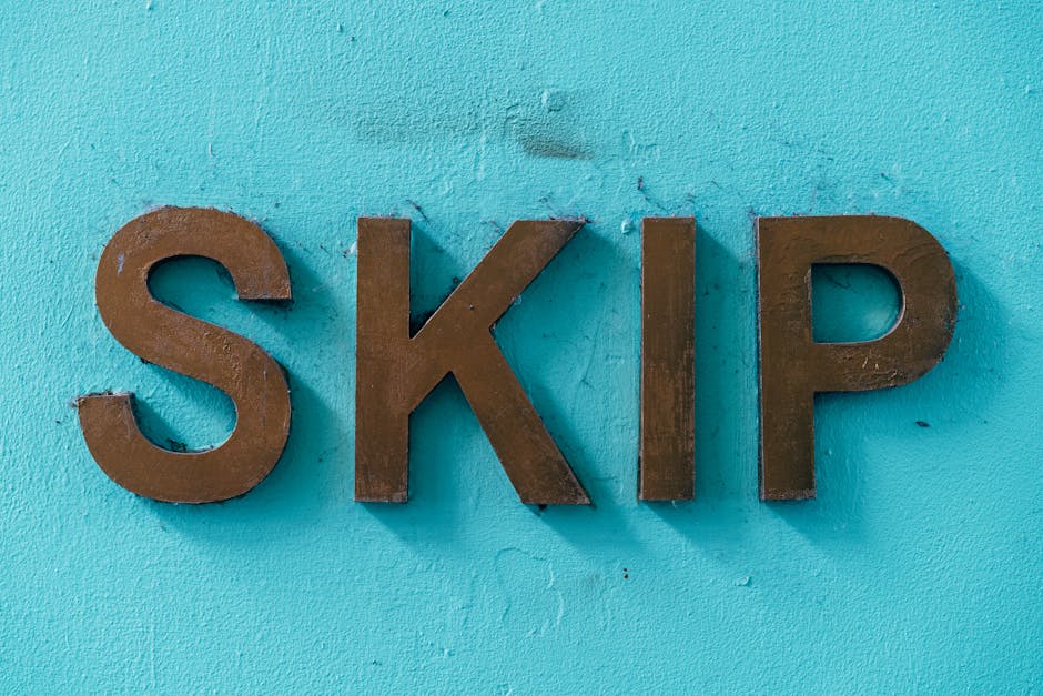 A close-up of three large, three-dimensional metallic letters spelling 'SKIP' mounted on a bright turquoise wall. The letters have a matte, slightly textured bronze finish with visible edges and subtl